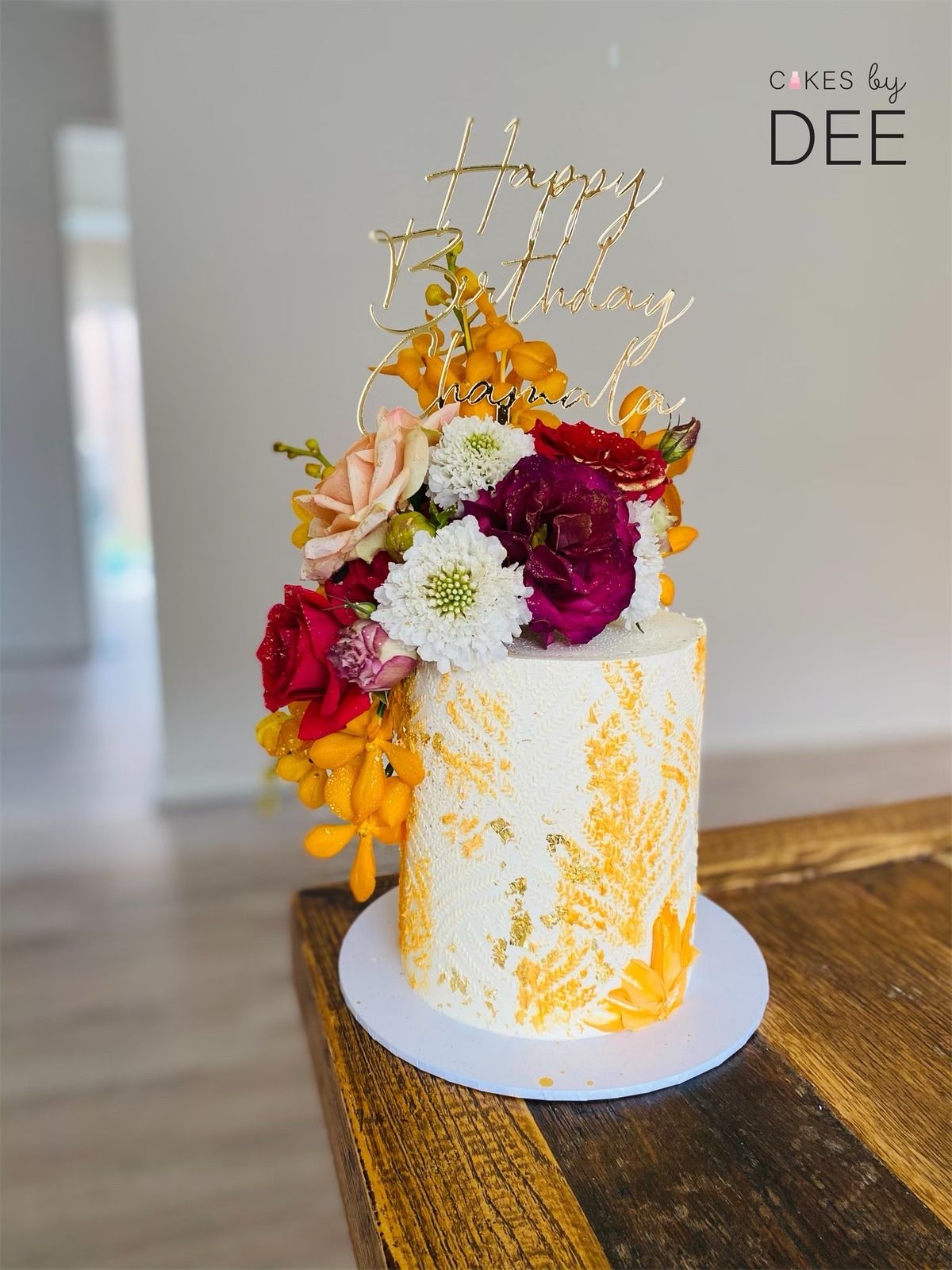 White textured birthday cake with gold splatters and fresh mixed real flowers including roses and chrysanthemums