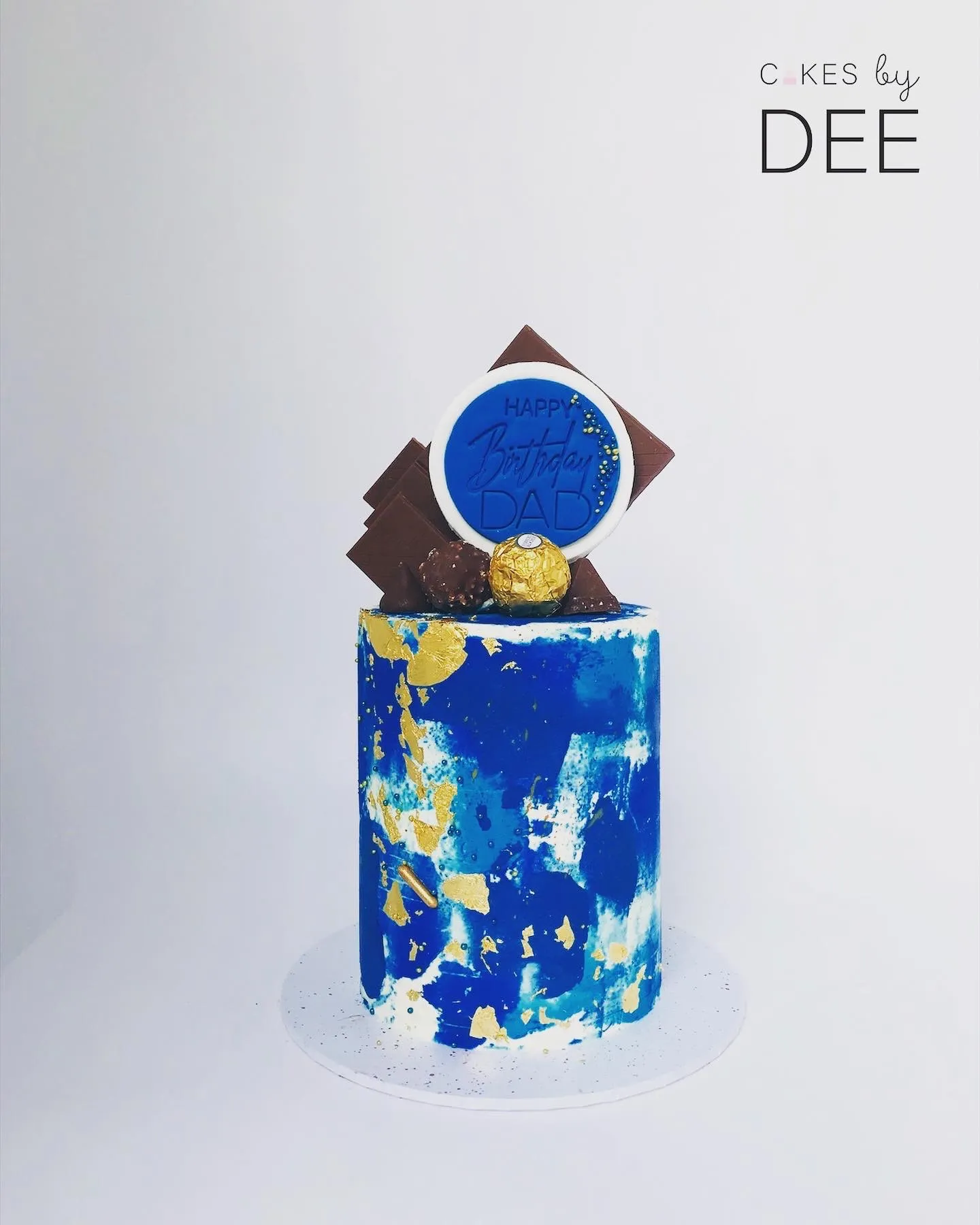Cylindrical abstract-painted blue and gold cake with Happy Birthday DAD disc topper and chocolate decorations