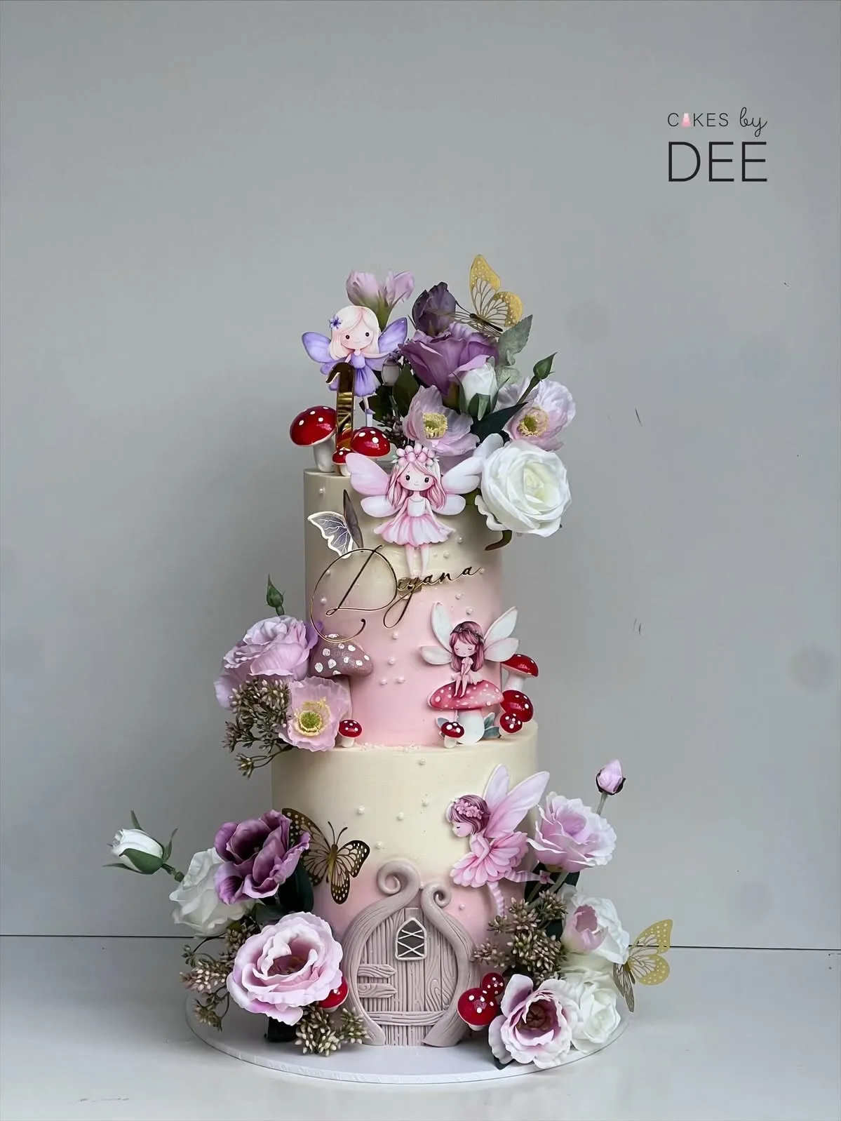 Three-tier fairy garden birthday cake for Deyana with hand-painted fairies, mushrooms, and cascading real flowers