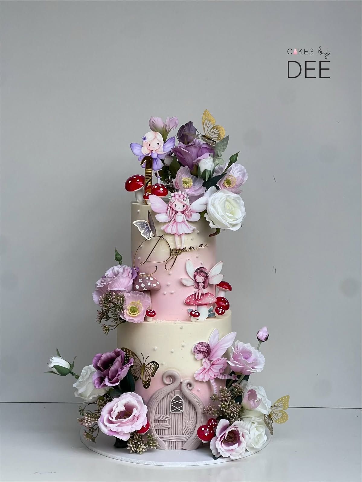 Three-tier fairy garden birthday cake for Deyana with hand-painted fairies, mushrooms, and cascading real flowers